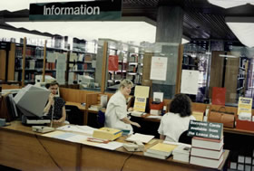Staff working at the information desk in the 1980s. The  microfiche catalogue is visible on the desk.
