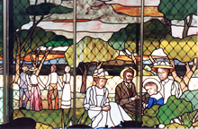 The stain glass window in the Drawing Room of the Rockingham Museum, depicting a family in a picnic type setting in the countryside.