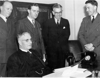 Prime Minister Curtin (seated) talking to senior journalists and press secretary, Don Rodgers (second from right) during a press briefing in Parliament House, Canberra.