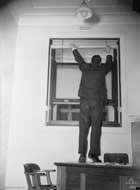 Parliament House staff implementing war precautions - fitting blackout blinds to a window, 1942